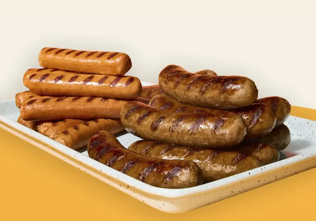 Selection of grilled sausages and frankfurters with char marks on a white platter, ideal for wholesale foodservice and food distribution suppliers.