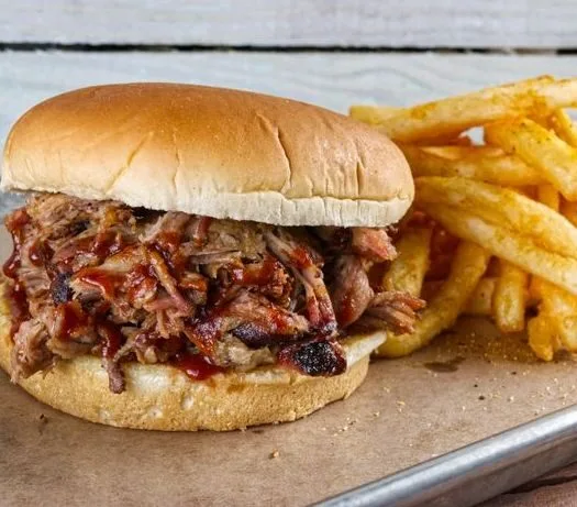 Delicious pulled pork sandwich with crispy fries on a rustic wooden background.