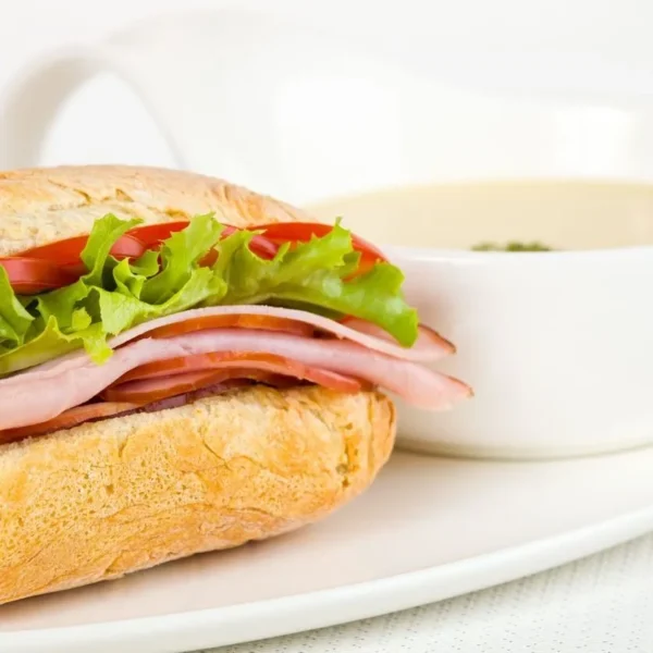 Freshly made sandwich with deli meats, crisp lettuce, tomatoes, and a side of creamy soup.